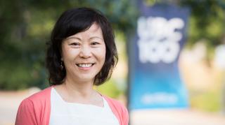 Photo of Phyllis Poon smiling in front of a UBC 100 flag